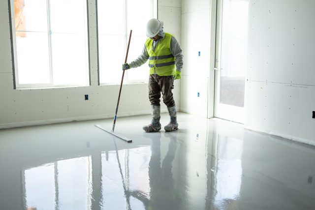 Finisher smoothing a fresh gypsum concrete pour by bright windows