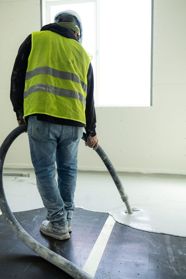 Worker directing the pour hose over acoustic mat