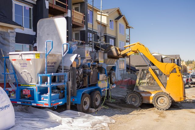 Skid steer loading sand into the GC-1 hopper in front of a three-story building