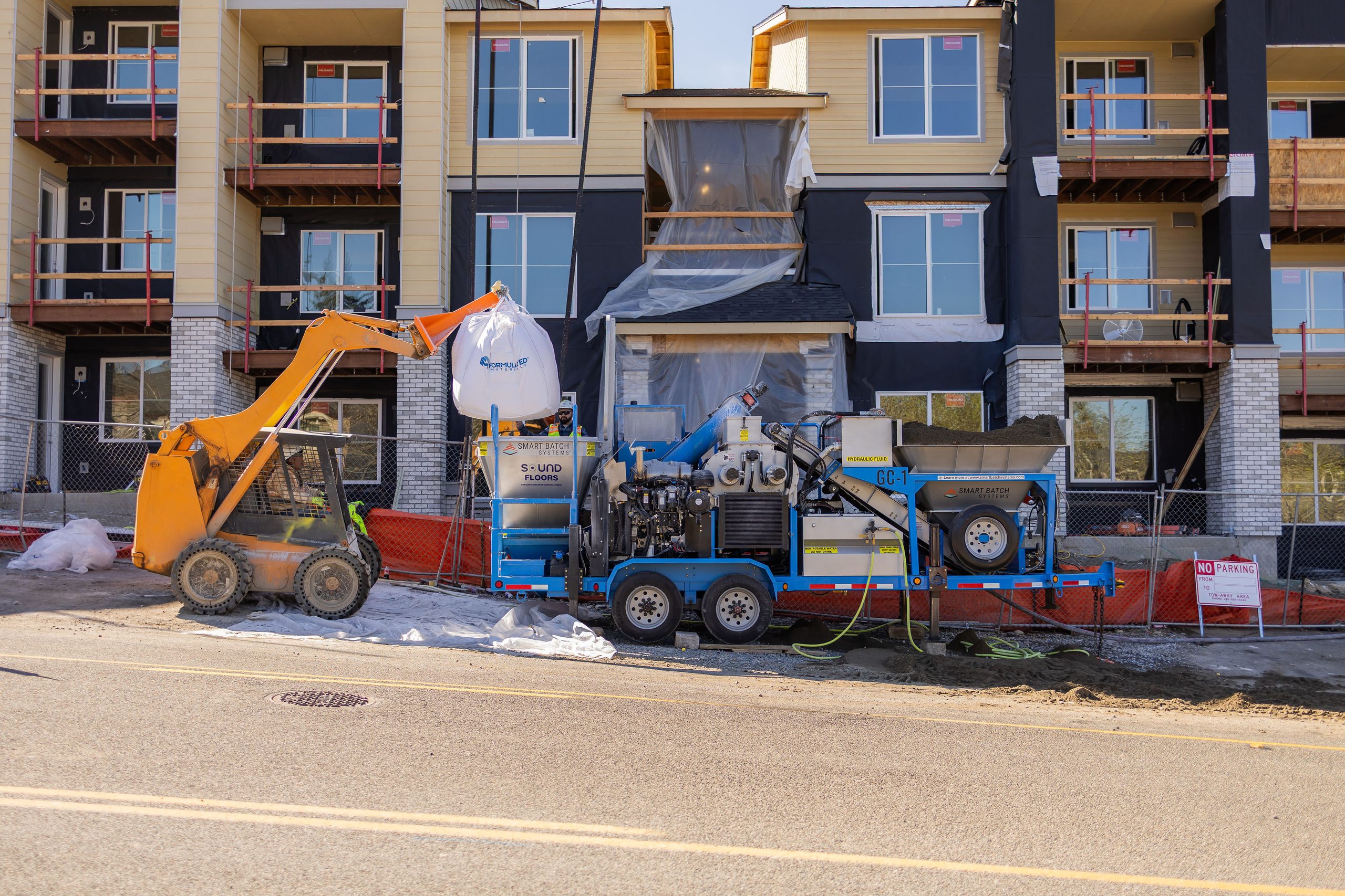 Smart Batch GC-1 rig and skid steer loading sand in front of a three-story multifamily building